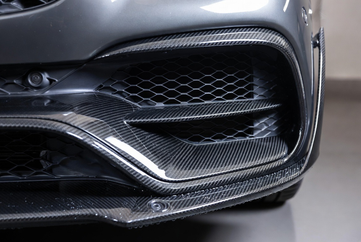 Close-up van een carbon Mercedes AMG-bumper met luchtinlaten en parkeersensoren
